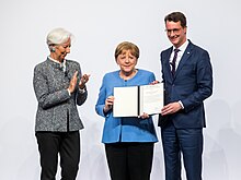 Merkel and a man holding the Bavarian Order of Merit while a woman claps.
