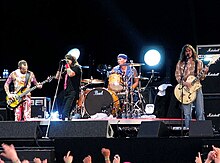 Fotografía de cuatro miembros de Red Hot Chili Peppers tocando en vivo