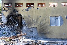 A wall of a building struck with an explosive, with other parts of the wall hit with bullets.