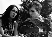 Fotografía en blanco y negro de Joan Báez y Bob Dylan cantando mientras este toca la guitarra