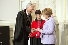 Merkel accepting a degree and shaking hands with a man.