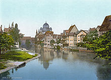 A postcard of a river with buildings behind it