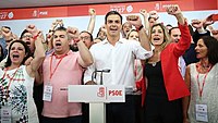 Pedro Sánchez wearing a white shirt and cheering with multiple people