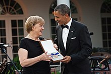 Angela Merkel and Barack Obama holding a presentation box with the Presidential Medal for Freedom