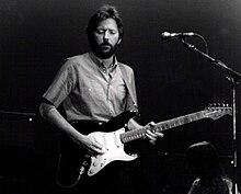 Fotografía en blanco y negro de Eric Clapton con una guitarra en escenario