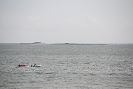 Vue en couleur d'une île plate en arrière plan d'une étendue d'eau, montrant deux barques.