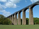 Looking up toward a metal aqueduct, supported by multiple tall, stone pillars and arches.