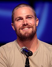 A photograph of Stephen Amell speaking at a convention behind a microphone