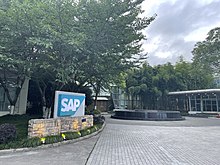樹蔭下，一處建築前的庭院，左側有一個藍底白字的「SAP」標誌