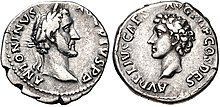 Pièce grise. À gauche, sur le recto, une tête d'homme barbu aux cheveux mi-longs et la mention Antoninus. Sur le verso, une tête d'un jeune homme aux cheveux frisés.
