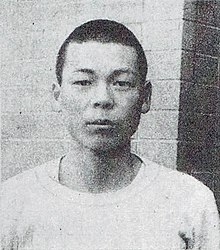A black and white film photo of a Japanese man with a neutral expression