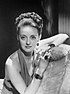 Portrait by George Hurrell of Bette Davis facing to the front, wearing a dress and holding a cigarette