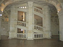 Photographie couleur d'un grand escalier circulaire intérieur, en élégante pierre blanche, au milieu d'un couloir lumineux et large de proportions.