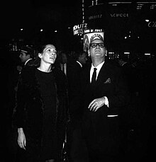 Photo en noir et blanc d'une femme et un homme dehors la nuit. En arrière-plan, la façade du cinéma Berlitz affiche en grandes lettres : « Hibernatus - Louis de Funès »