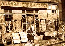 Dentellière devant son commerce au Puy, vers 1930.