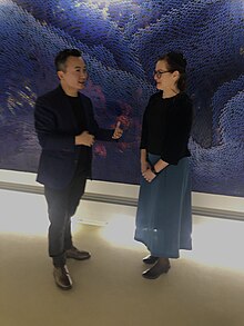 Photo couleur d’un homme et d’une femme devant un tableau bleu.