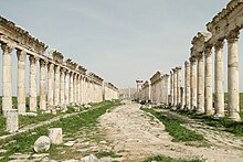 A view of road lined with columns, some of which are still topped with a decorative frieze