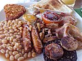 全套的英式早餐包含炒雞蛋，香腸，黑布丁，培根，蘑菇，烤豆，薯餅和半西紅柿