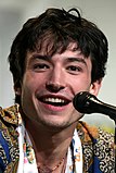 A photograph of Ezra Miller speaking at a convention behind a microphone