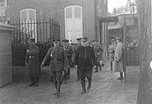 Deux généraux, Haig en uniforme britannique et Joffre en uniforme français, suivis par d'autres officiers, sortent par le portail d'une villa en brique