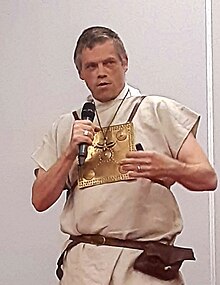 Ben Kane wearing a Roman outfit, appearing to speak into a microphone