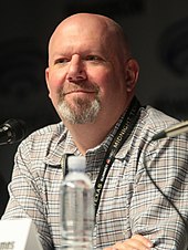 A photograph of Marc Guggenheim speaking at a convention