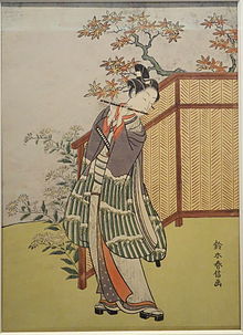 A young man wearing a long-sleeved kimono and sandals playing the flute.