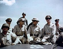 Huit hommes assis en uniformes kakis