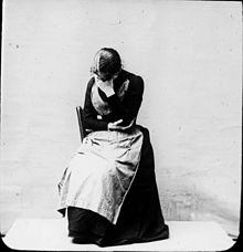 Photographie d'une femme assise, la tête courbée, le visage caché dans une main
