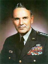 Middle-aged man with graying dark hair parted slightly off center. He wears a green dress uniform, with suit and tie, is clean-shaven, and has four stars on his shoulder to indicate his rank.