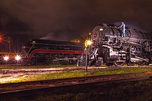 Two steam locomotives at night with a man standing on the right locomotive