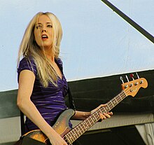 A 32-year-old woman is playing a four-string electric bass guitar.